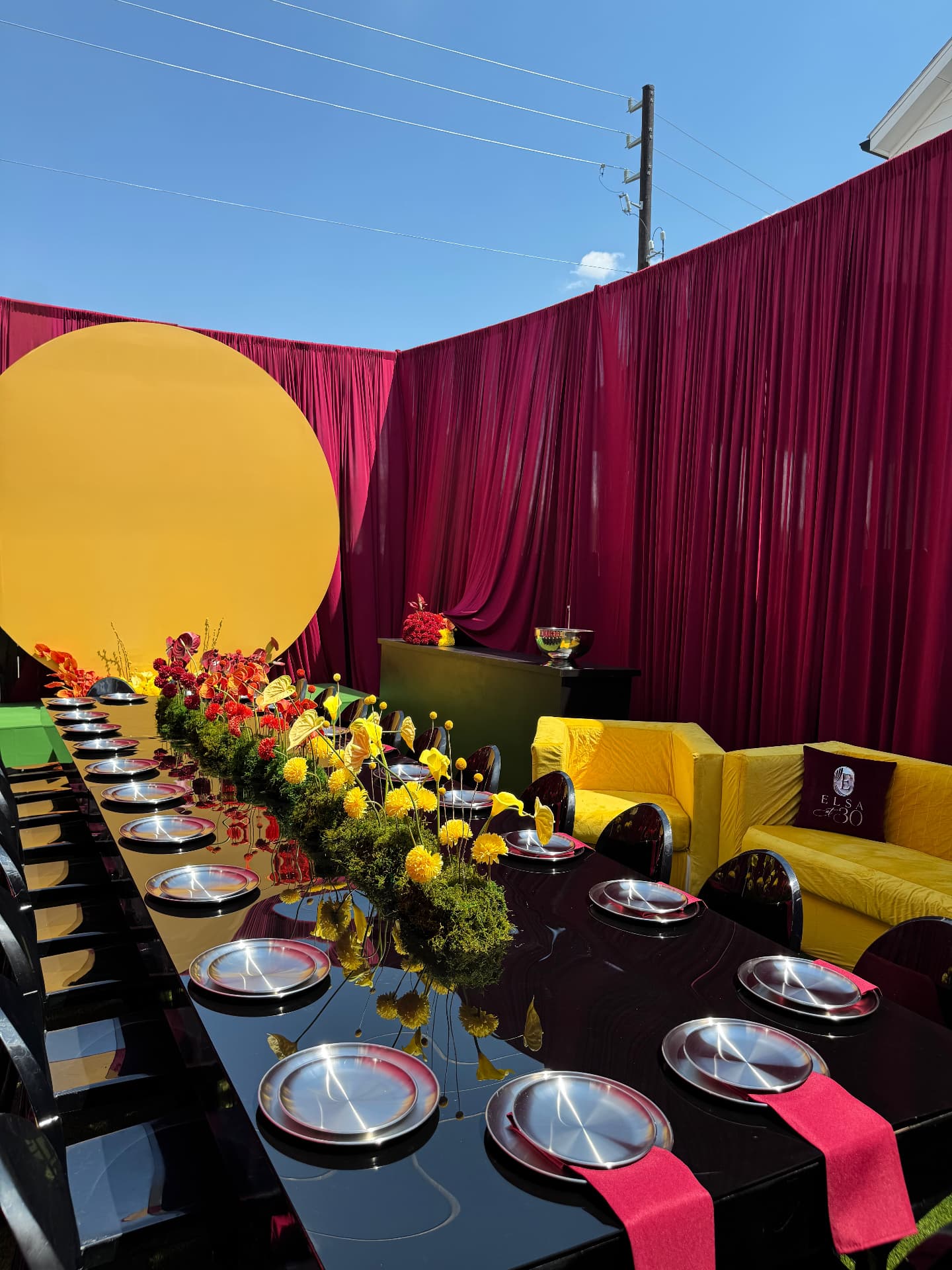 Burgundy draped dinner scene with a bold yellow circular backdrop and mirrored tablescape in Houston