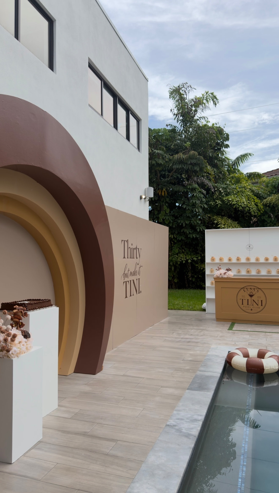 Chocolate and tan layered arch backdrop with white plinths at the birthday pool club