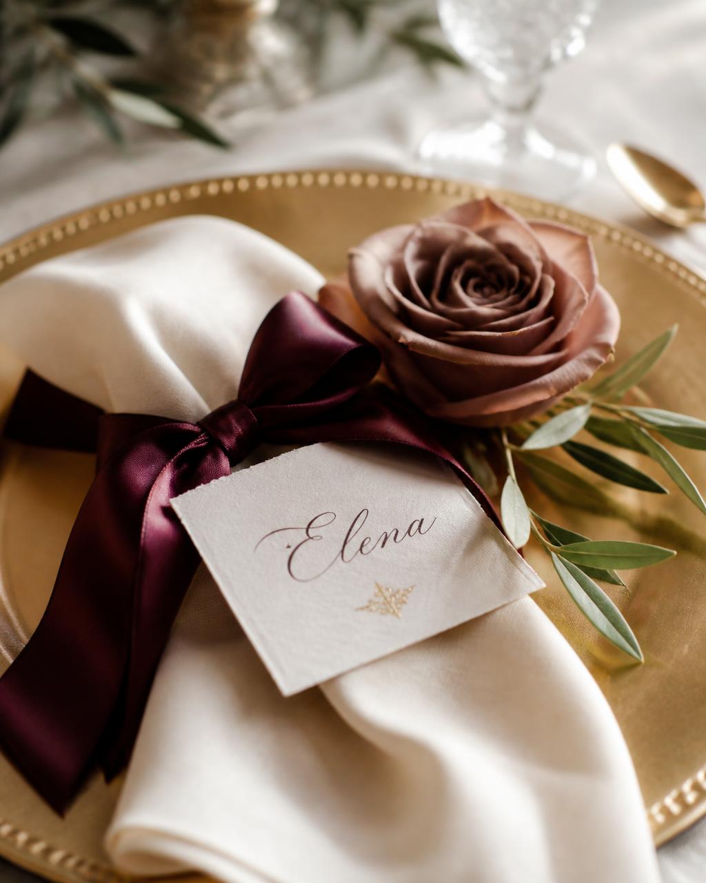 Place setting with cream napkin, burgundy ribbon and a mocha rose