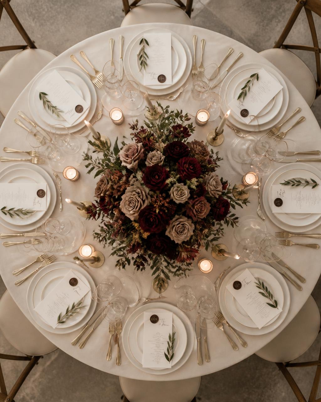 Overhead view of a round wedding table with a low burgundy centrepiece